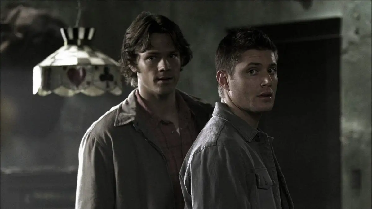 Sam & Dean in "Supernatural" stand in dark room and look nervously into the distance.