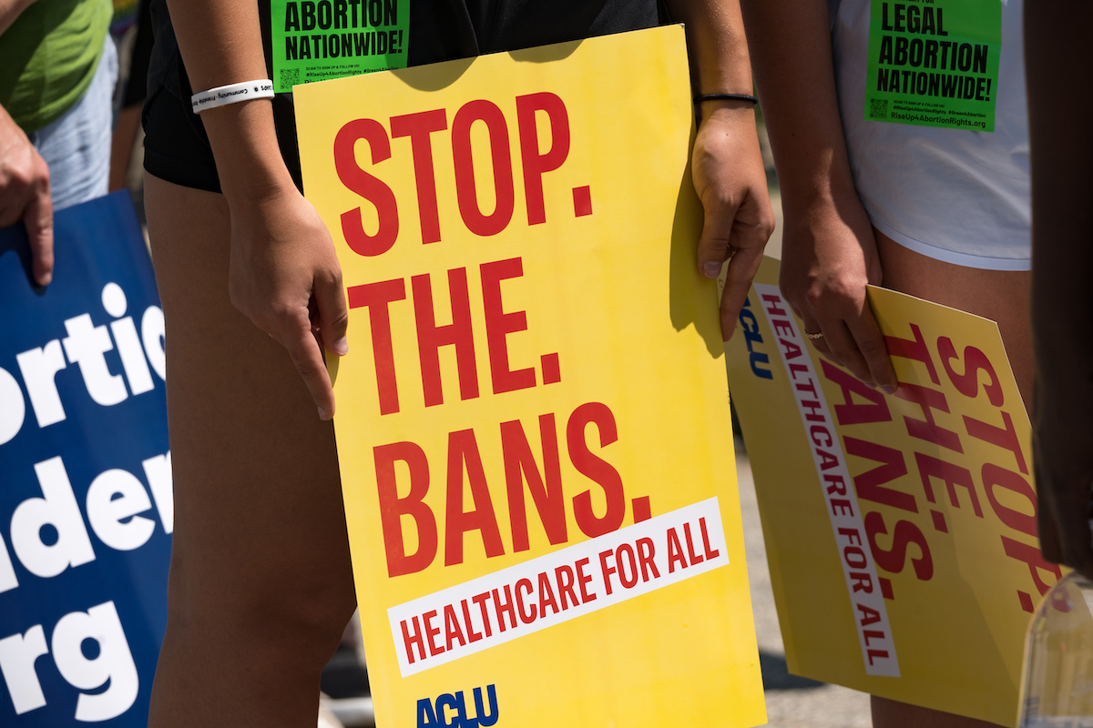 A protester holds a sign reading "STOP THE BANS"