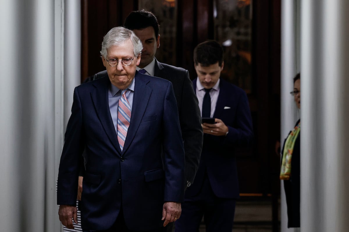 Mitch McConnell bites his lip and looks down as he walks with aides behind him.
