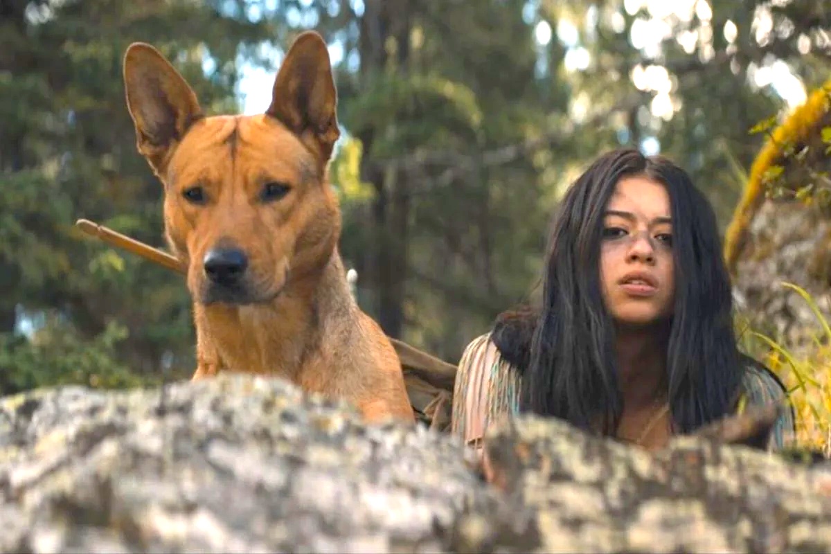 Amber Midthunder as Naru looking over the edge of a cliff with her dog. Image: Hulu.
