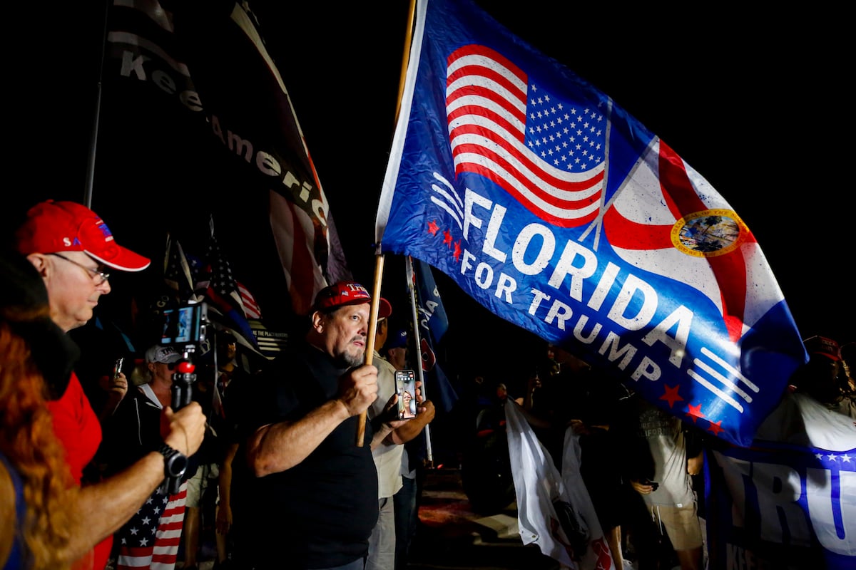 Trump's supporters protest outside at night, holding flags reading "Florida for Trump"