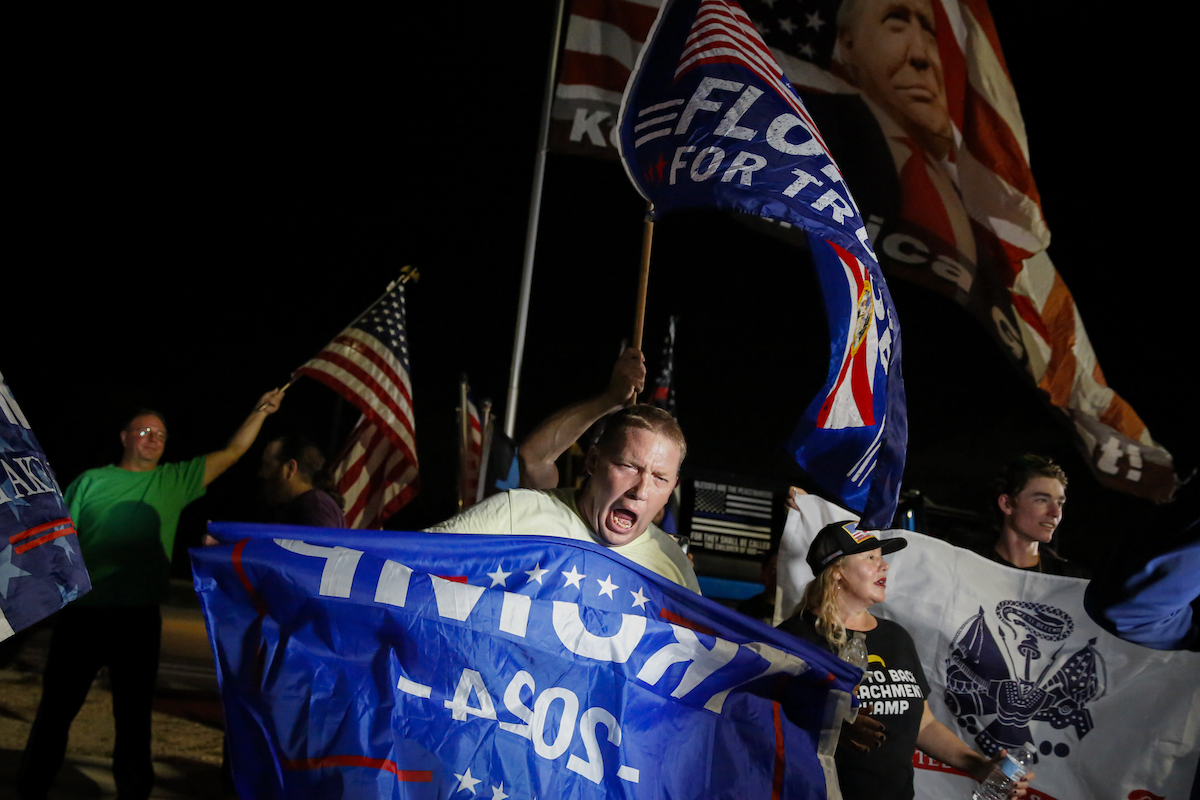 Trump supporters hold signs and flags and yell.