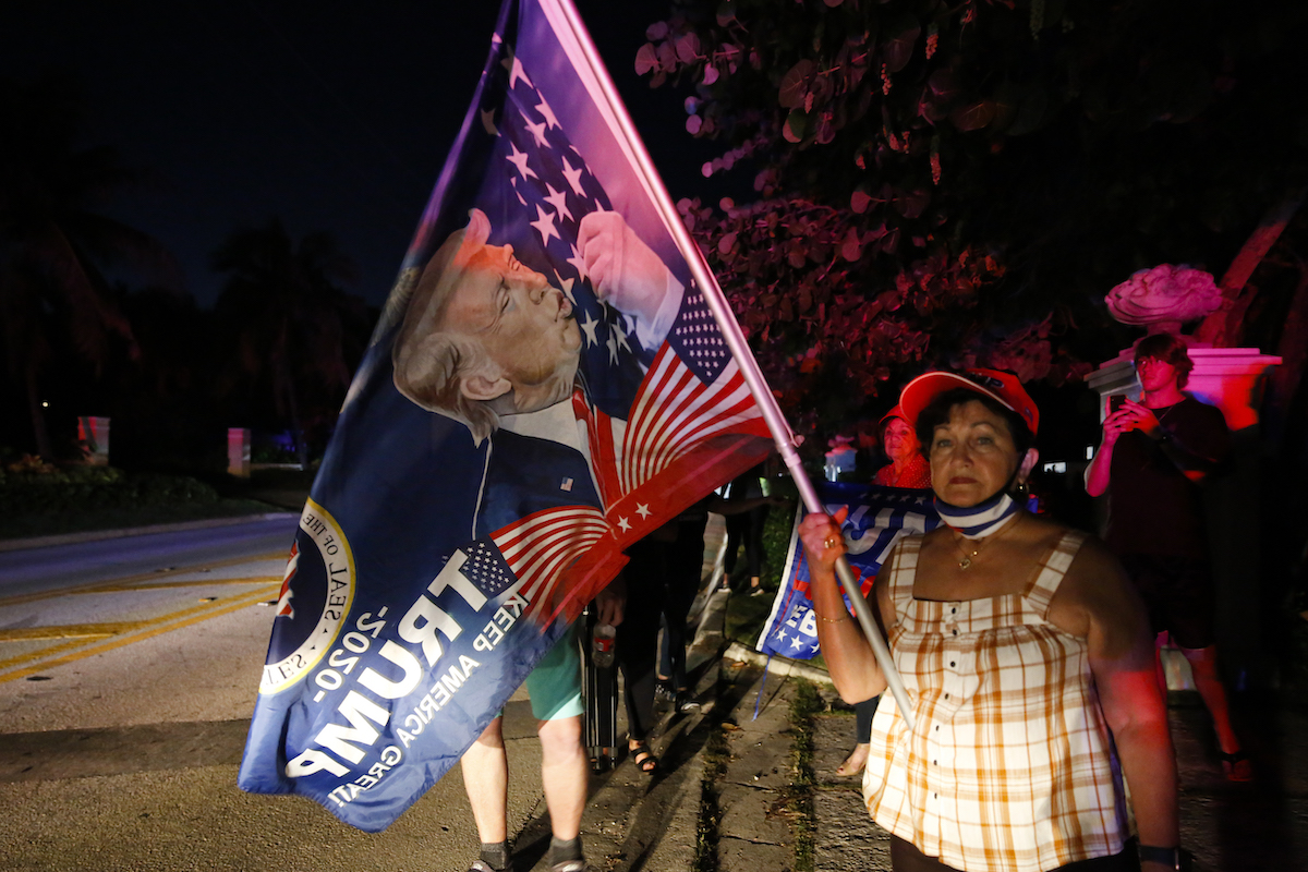 A woman holds a giant Trump flag outside at night.