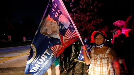A woman holds a giant Trump flag outside at night.