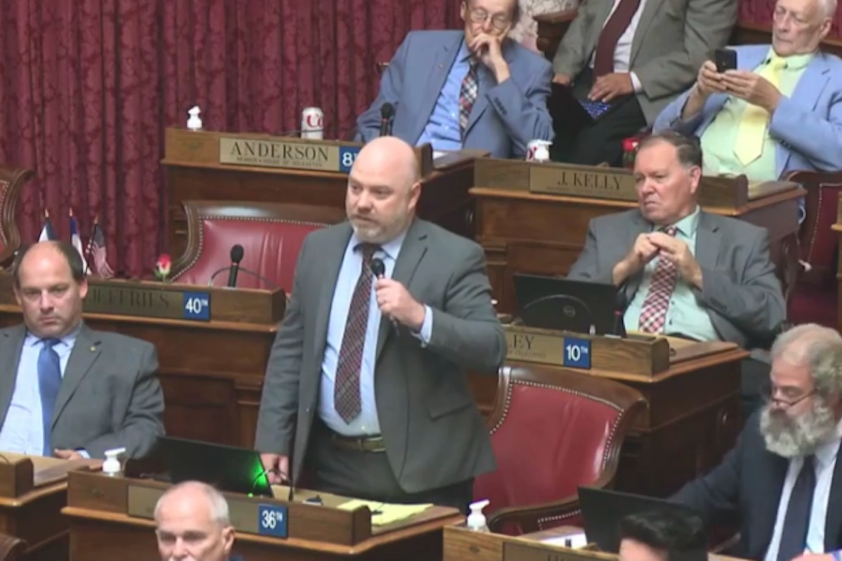 A middle aged white man stands and speaks, surrounded by other white men, in the West Virginia statehouse.