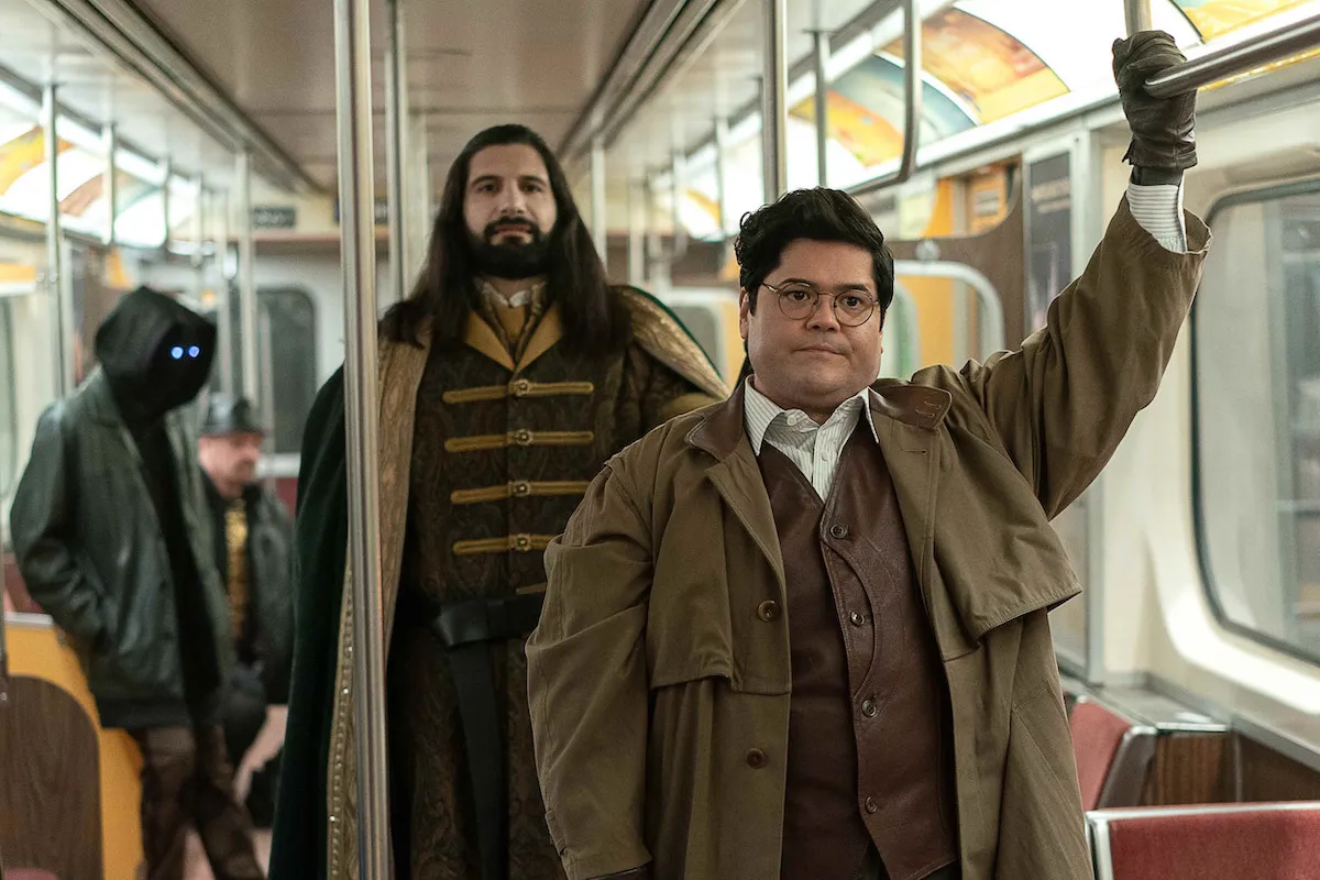 Guillermo and Nandor stand in a subway car. Guillermo looks annoyed.