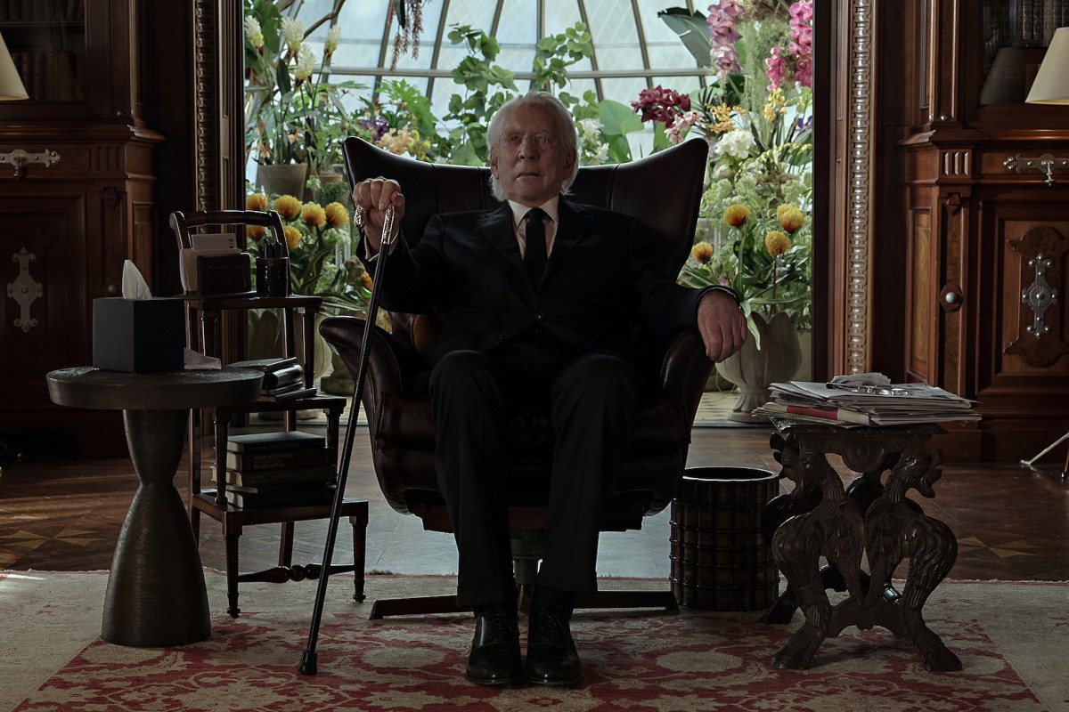 An imposing older man sits on a chair.