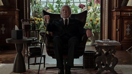 An imposing older man sits on a chair.