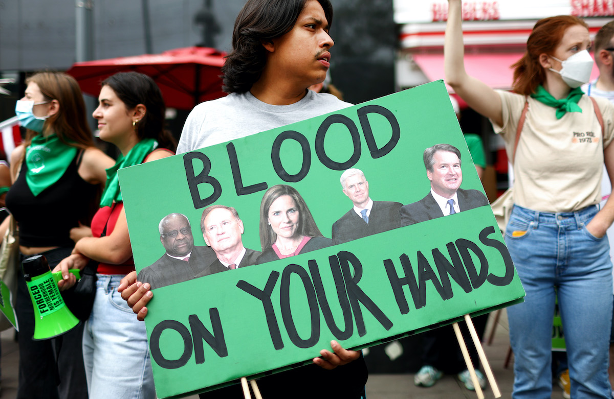 A protester holds a sign featuring the pictures of the conservative supreme court justices and the words "blood on your hands."