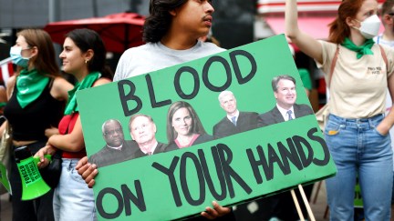 A protester holds a sign featuring the pictures of the conservative supreme court justices and the words 