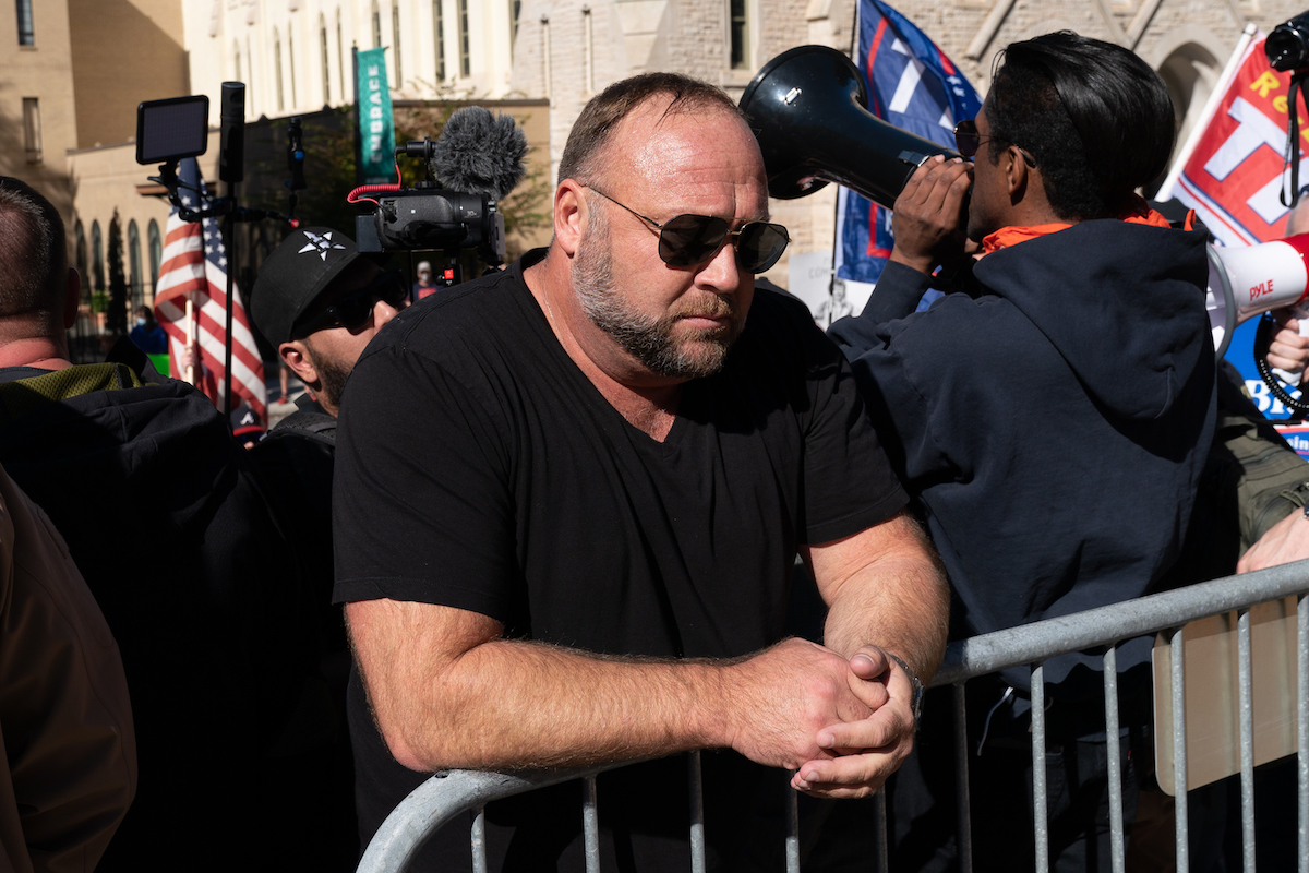 Alex Jones leans against a metal railing looking sad during a rally.