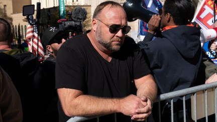 Alex Jones leans against a metal railing looking sad during a rally.