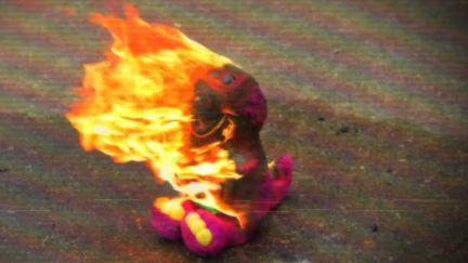 A Barney doll on fire on the road. Image: Peacock.