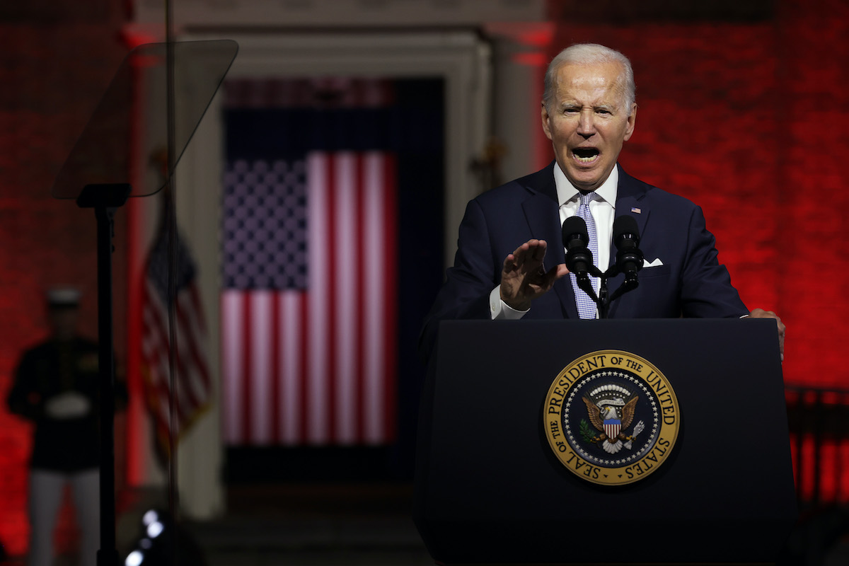 Joe Biden speaks passionately from a podium in front of a deep red background and an American flag