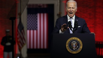 Joe Biden speaks passionately from a podium in front of a deep red background and an American flag