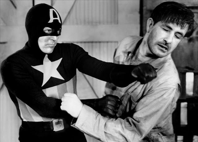 Captain America punches a bad guy in a black and white film.
