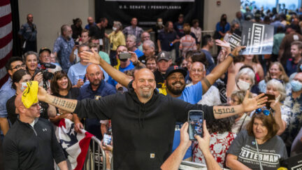 John Fetterman spreads his arms wide and grins standing in front of a crowd of supporters