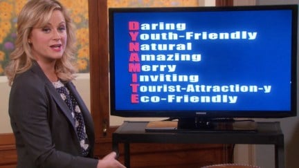 Leslie Knope stands in front of a presentation screen with acrostic 