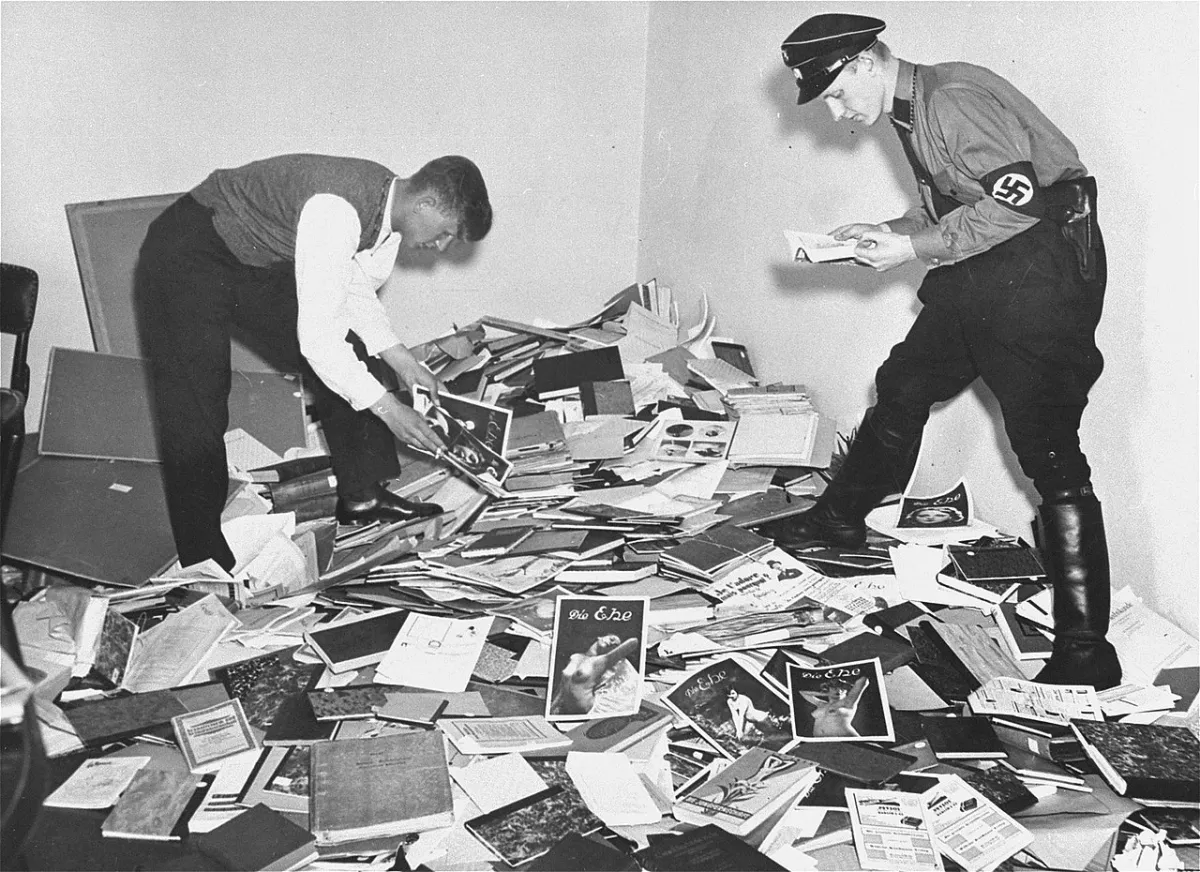 A uniformed member of the Nazi SA and a student of the Academy of Physical Exercise examine materials plundered from the library of Dr. Magnus Hirschfeld, director of the Institute for Sexual Science in Berlin on May 6, 1933. While some materials were burned immediately on the street outside the Institute, others were loaded onto trucks and carted away for sorting. Some were torched at the ceremonial book burning on Berlin's Opera Square on May 10, but selected valuable antiquarian books and periodicals were actually sold abroad. Manfred Baumgardt, Schwules Museum Berlin. Image: public domain