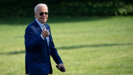 Joe Biden gives a thumbs up to the camera while walking across the white house lawn.