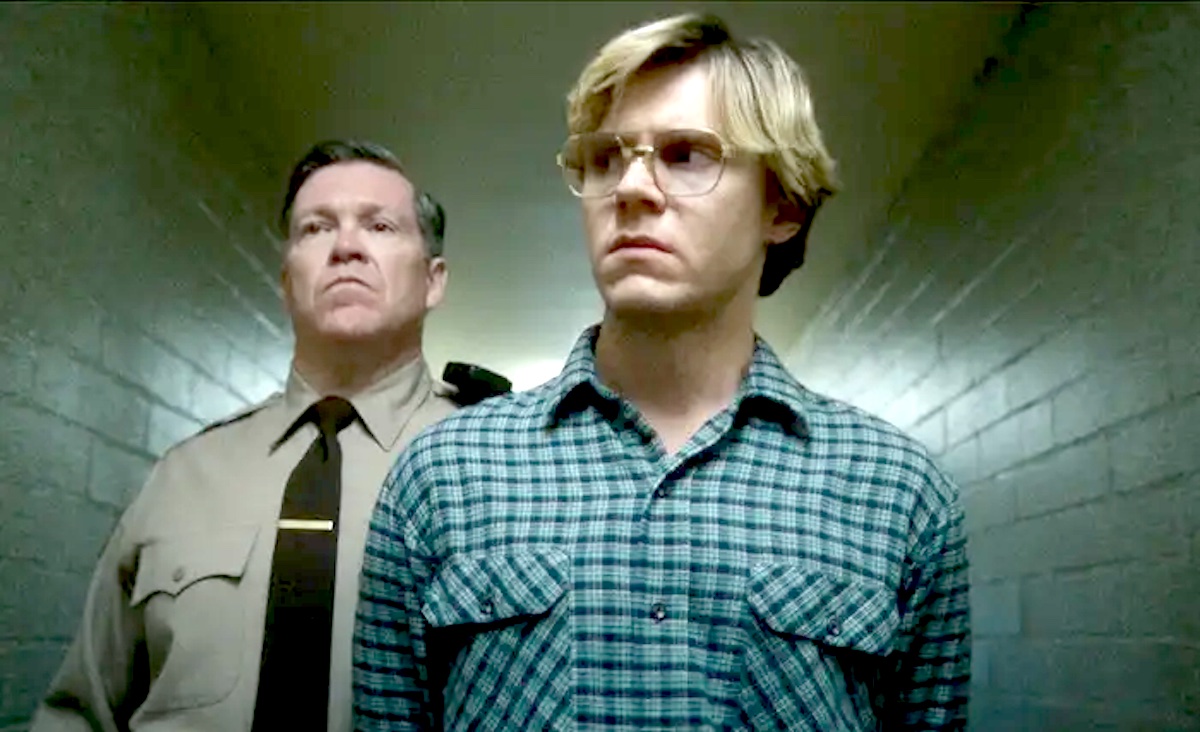 Evan Peters as Jeffrey Dahmer in Netflix's Monster series, being escorted down a hallway by a policeman.