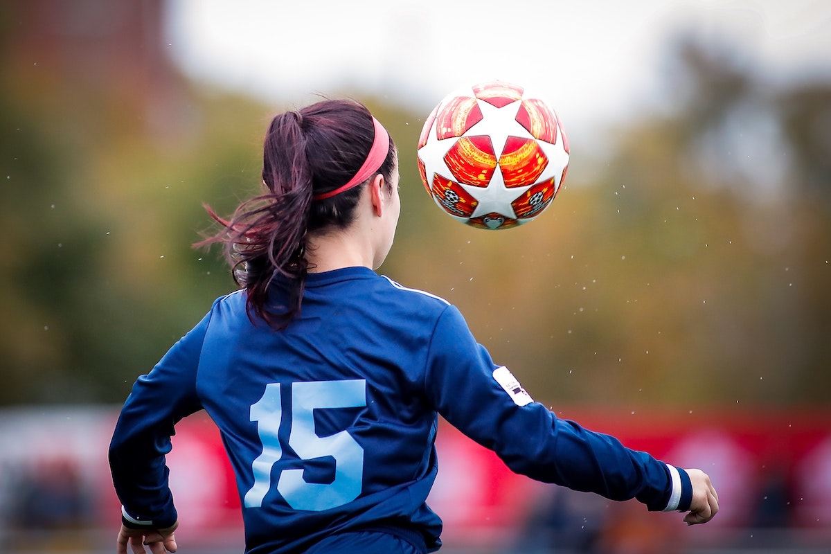 Seen from behind, a girl concentrates on a soccer ball in the air in front of her.