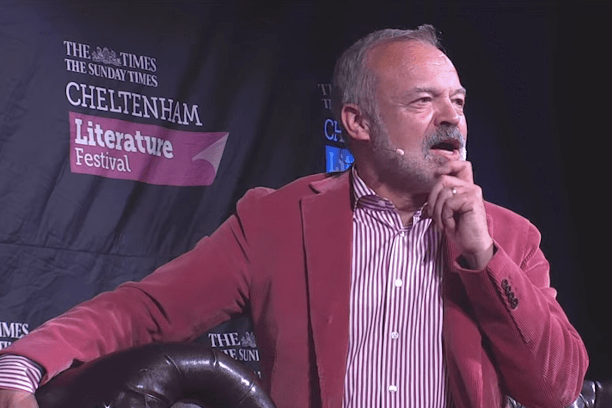 Graham Norton speaks at an event, wearing a pink suit, posing with his hand on his chin as he talks.