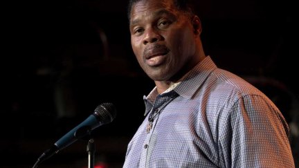 Herschel Walker looks to the side, into the camera, while standing at a microphone.