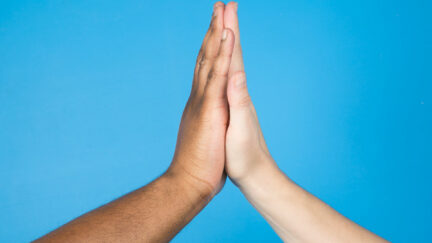 Two hands high five in front of a blue backdrop.