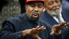 Kanye West (Ye) wears a red MAGA baseball hat and gestures while talking.