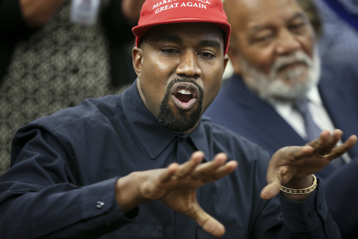 Kanye West (Ye) wears a red MAGA baseball hat and gestures while talking.