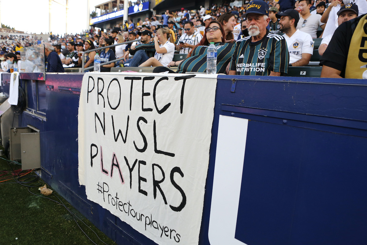 A handwritten banner reading "Protect NWSL Players" hangs in the stands at a soccer game.
