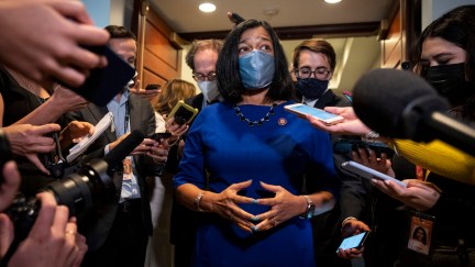 Democratic Rep. Pramila Jayapal stands wearing a mask, surrounded by a horde of reporters holding phones, microphones, and cameras in her face.