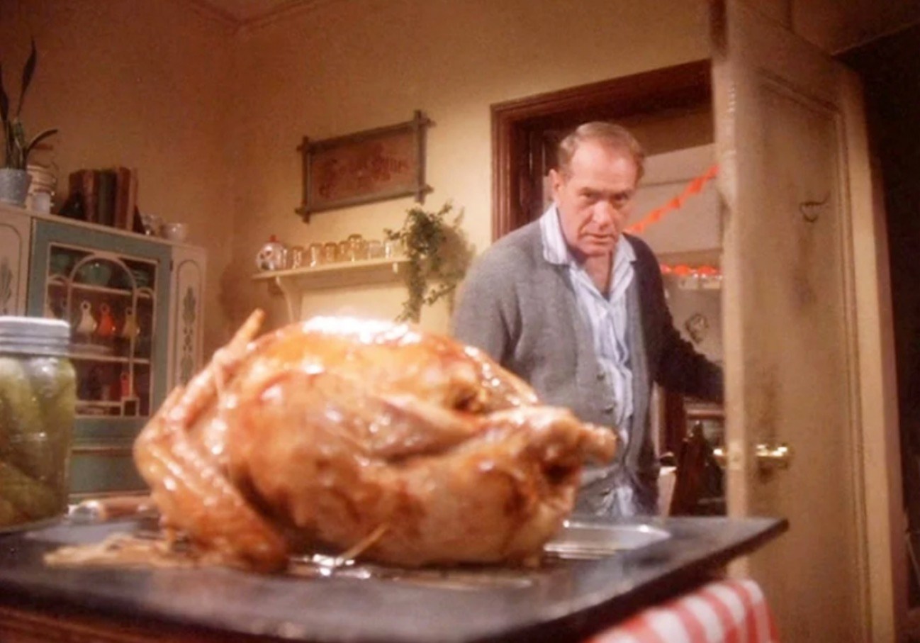 An older man eyes a delicious looking turkey sitting on a kitchen table in a scene from A Christmas Story.
