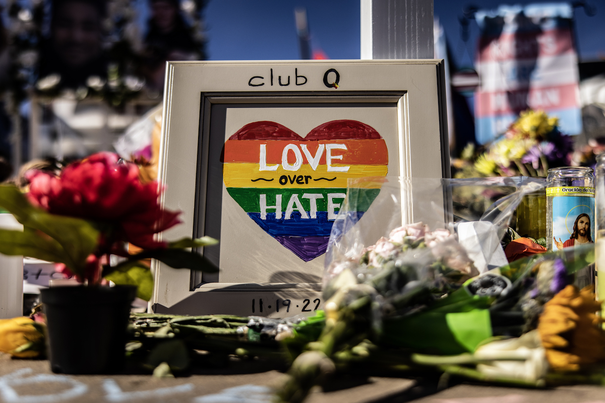 A memorial with flowers and a framed picture of a rainbow heart, with club q written on the frame