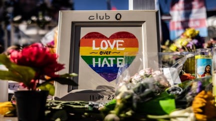 A memorial with flowers and a framed picture of a rainbow heart, with club q written on the frame