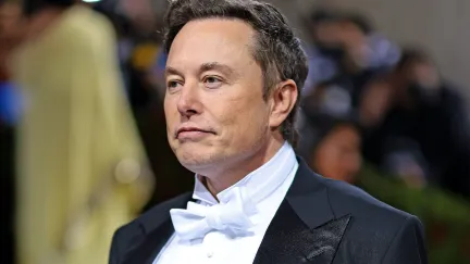 Elon Musk frowns slightly wearing a tux on a red carpet.