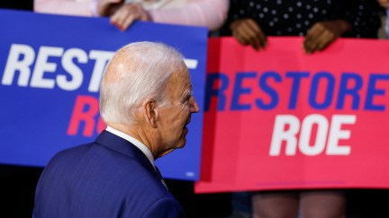Joe Biden walks away from the camera, toward the crowd behind him holding signs reading 