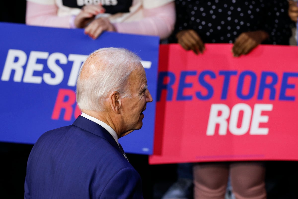 Joe Biden walks away from the camera, toward the crowd behind him holding signs reading "restore roe"