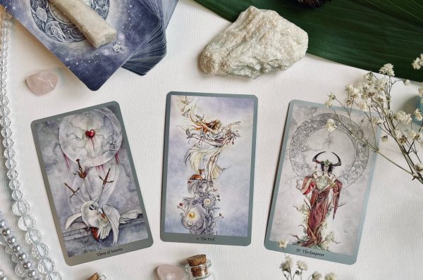 Three Stephanie Law Shadowscapes tarot cards laid out on a table with herbs and crystals.