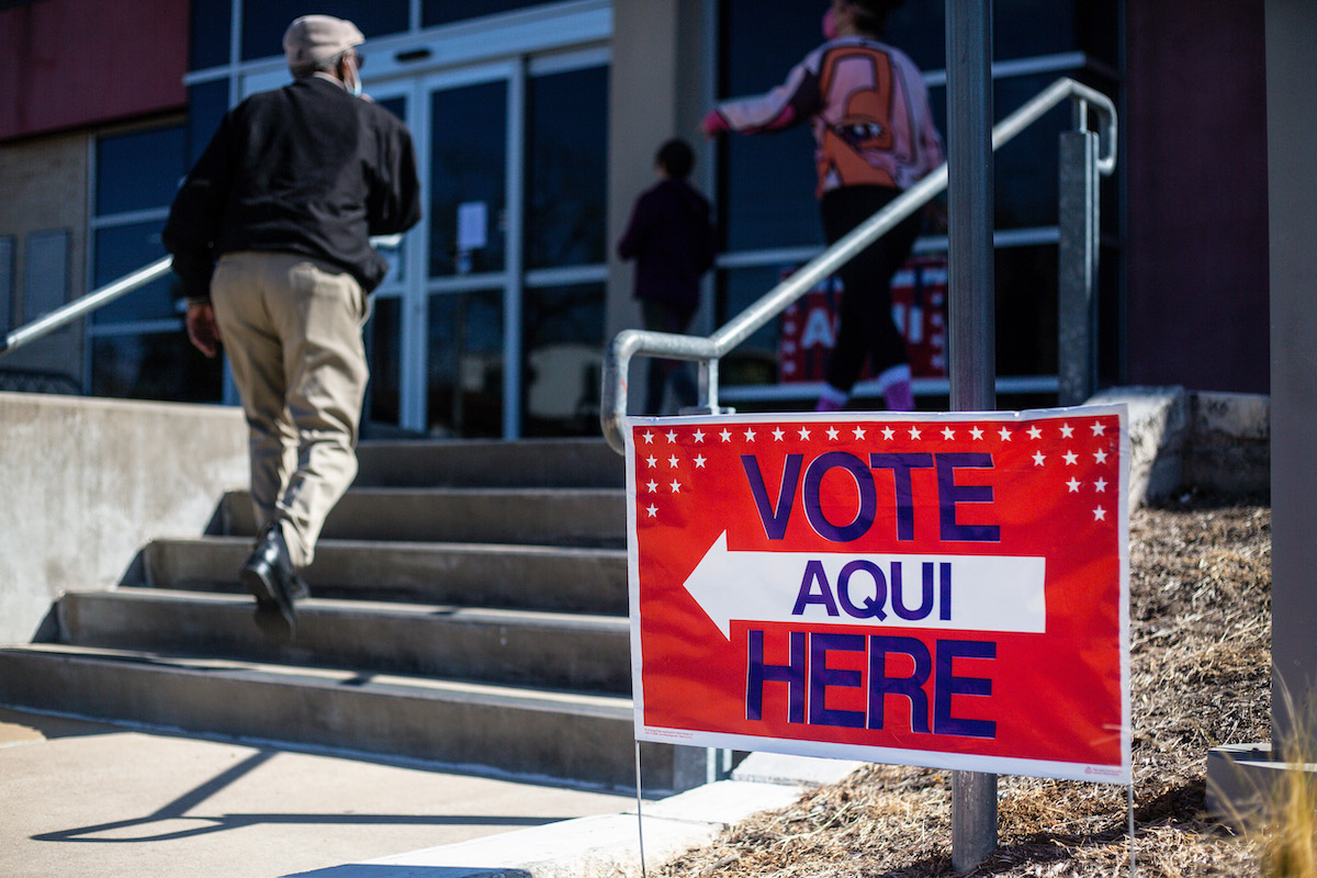 People enter a building with a sign outside reading Vote (aqui) here