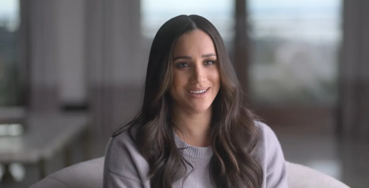 Meghan Markle sits on a couch and smiles in 'Harry & Meghan.'