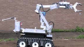 The ANDROS Wolverine V2 robot, a small white device with treads and a long gripper arm.