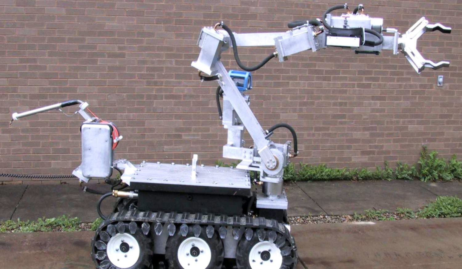 The ANDROS Wolverine V2 robot, a small white device with treads and a long gripper arm.