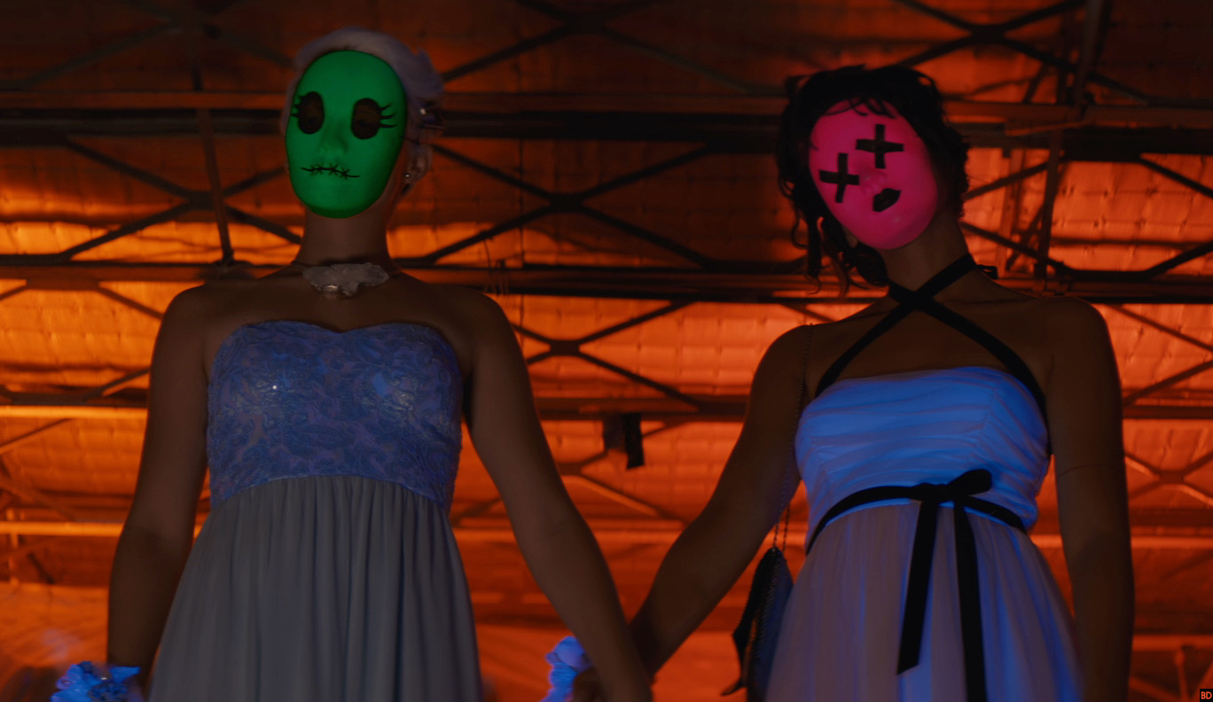 Sadie (Brianna Hildebrand) and McKayla (Alexandra Shipp) wear creepy neon masks and formal dresses to a school dance in 'Tragedy Girls'