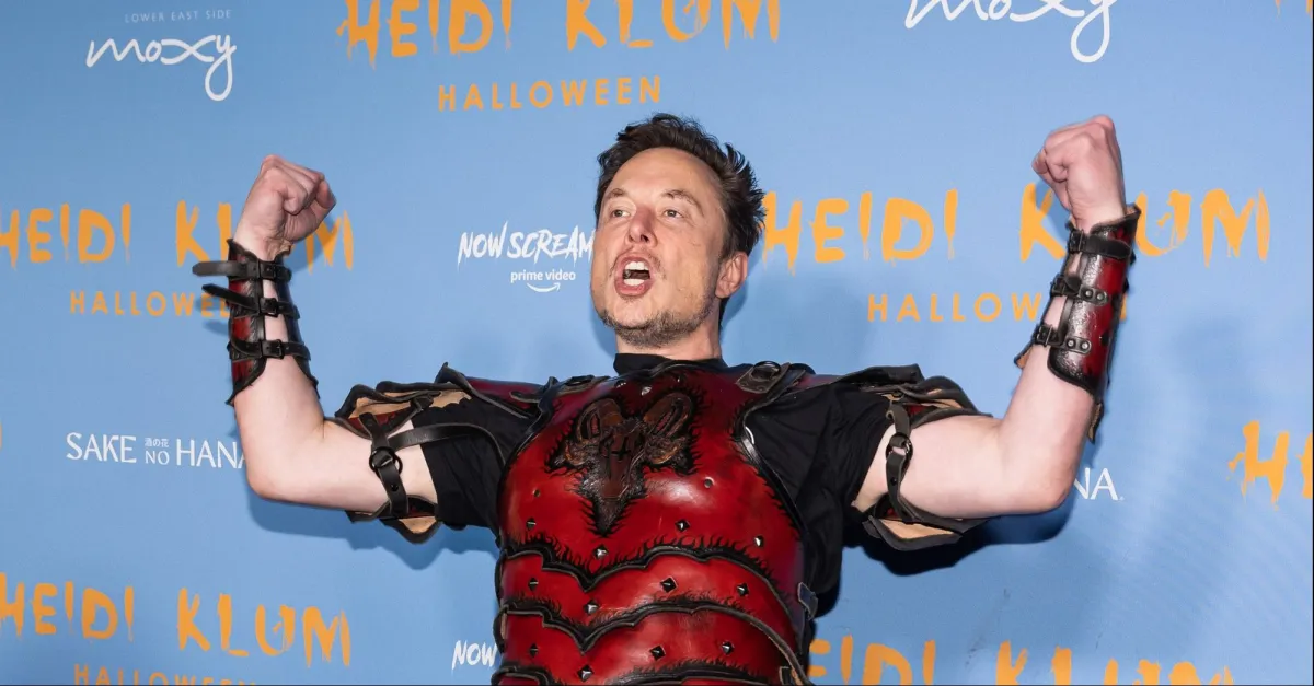 Elon Musk raises his arms and yells, wearing a Halloween costume consisting of red armor.