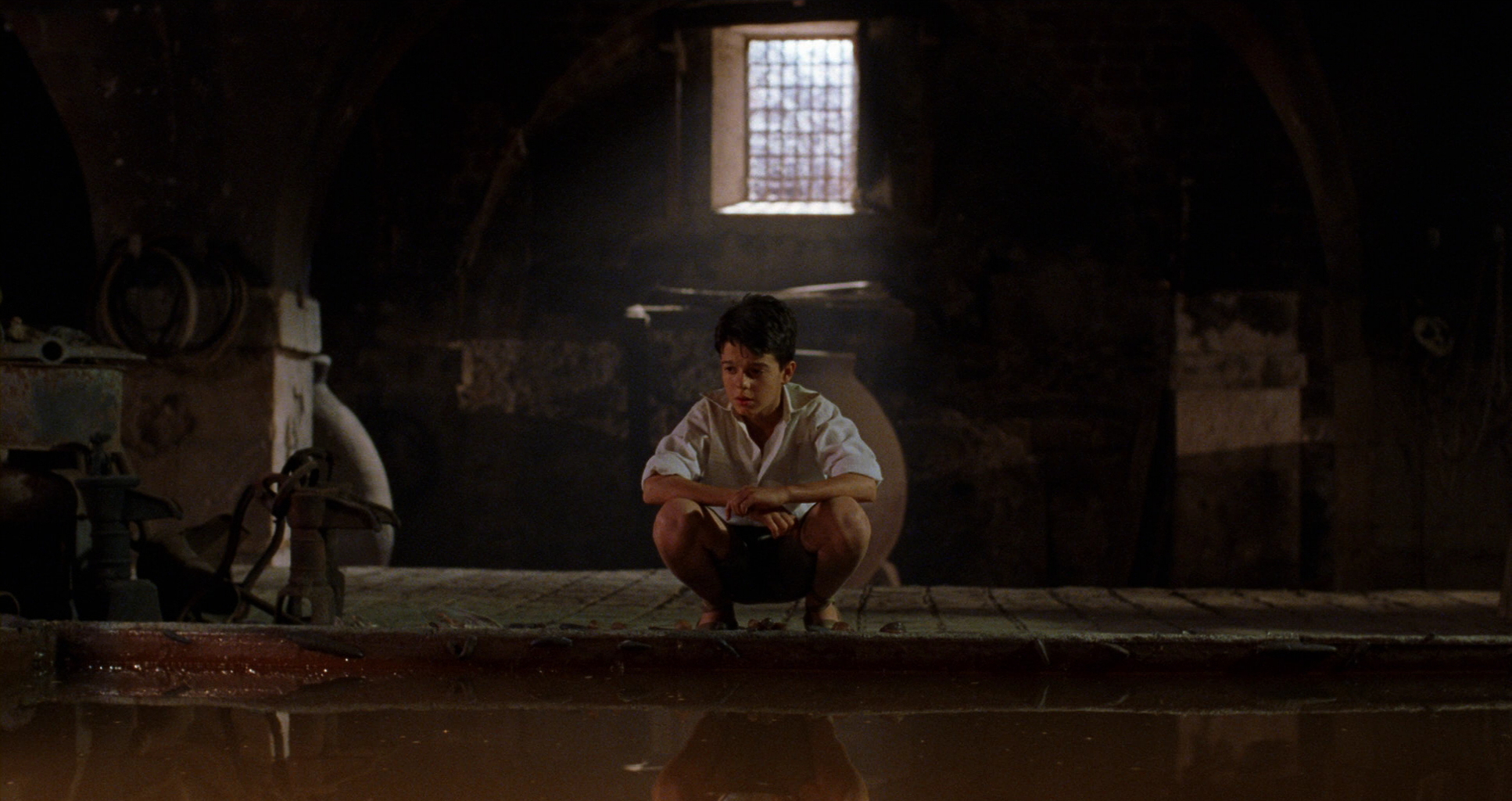A young boy crouches over a brackish pool of water in a scene from 'The Devil's Backbone'