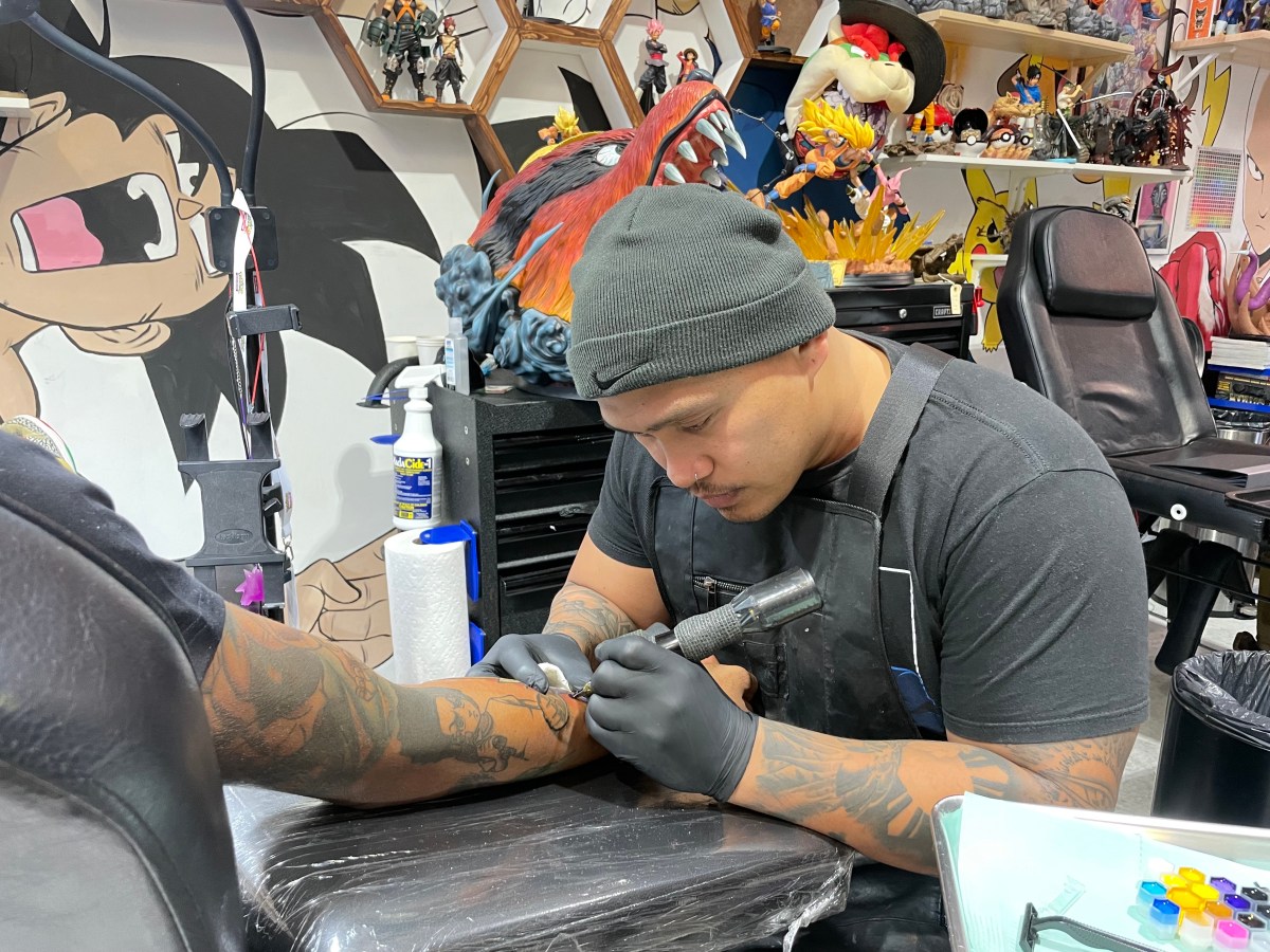 A tattoo artist wearing a grey beanie works on someone's arm.