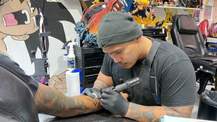 A tattoo artist wearing a grey beanie works on someone's arm.