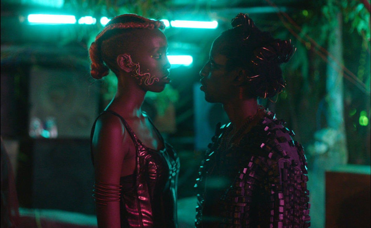 Two women standing face to face in a darkened room with neon lights in the background, from "Neptune Frost"